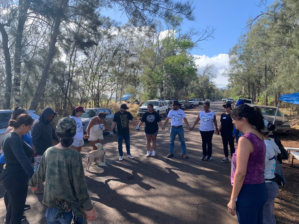 Community members holding hands in a circle before a Holomua Road cleanup