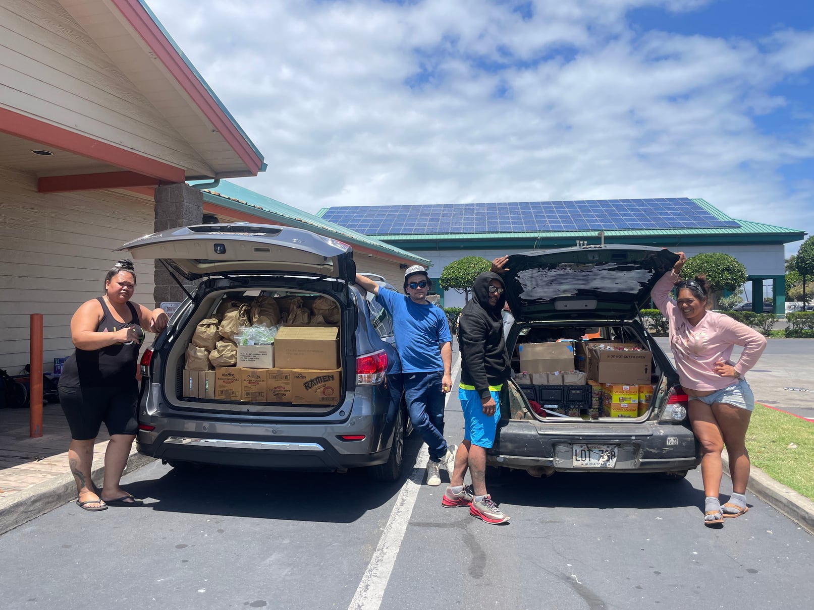 Holomua Outreach volunteers beside vehicles loaded with food and essential care supplies